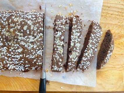 Biscotti log being sliced showing the knife completely perpendicular to the cutting surface, not canted, in order to yield the straightest sides.